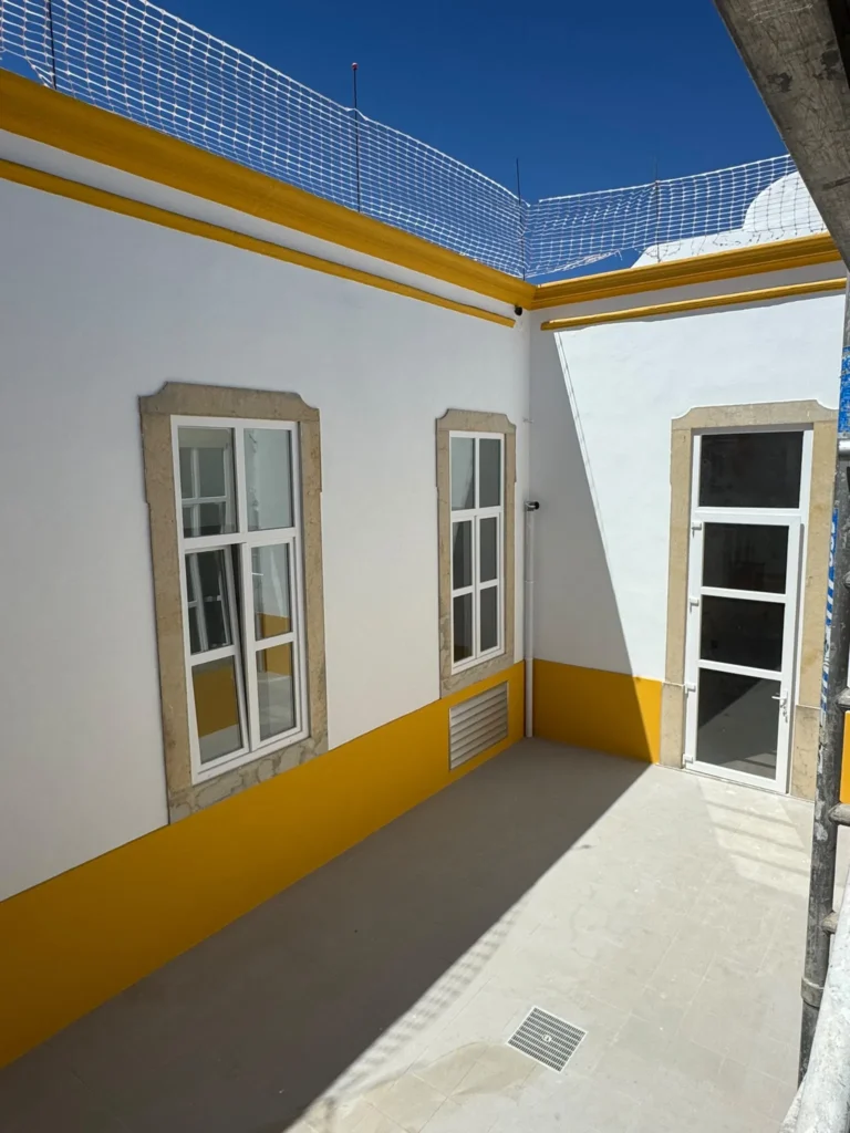 Pátio interior com friso amarelo e janelas em PVC branco