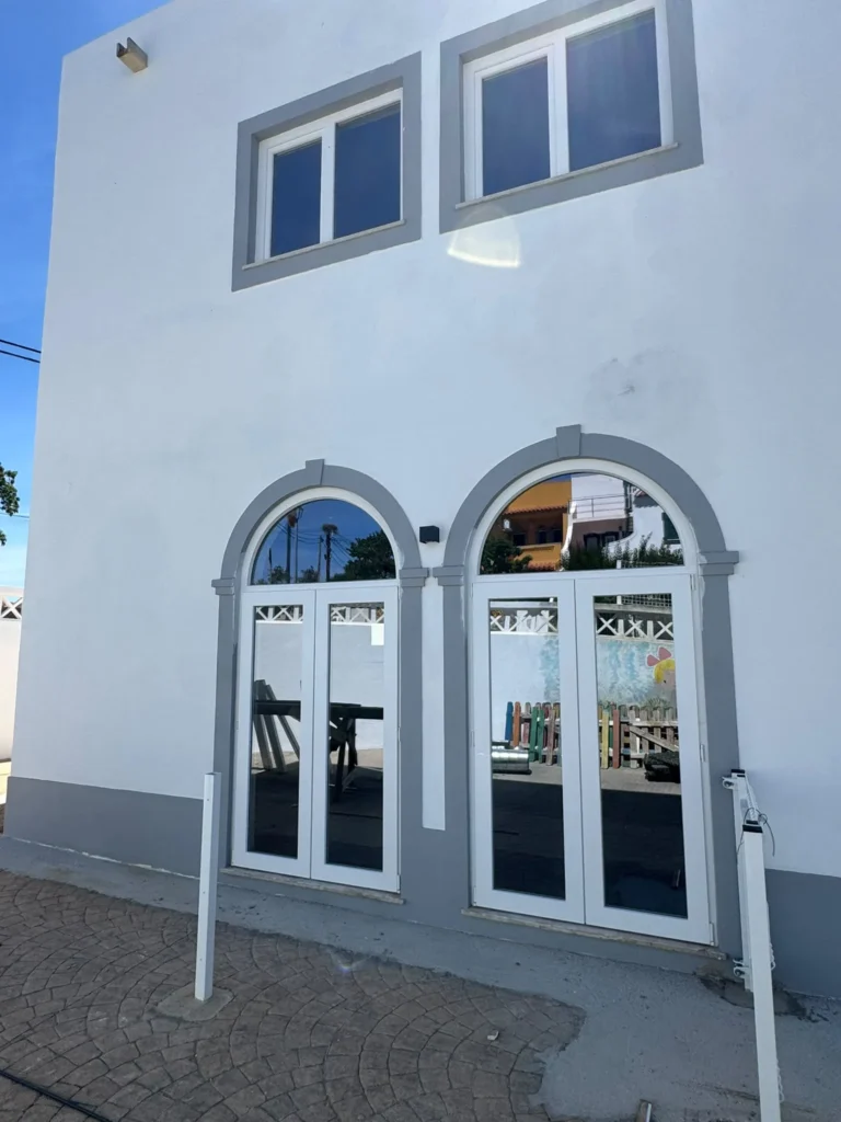 Fachada branca com duas janelas em arco e portas envidraçadas em PVC